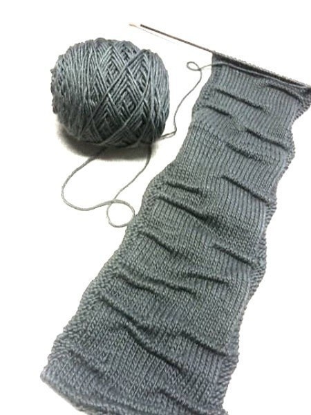 Оригинальный вязаный шарф выполнен спицами текстурной вязкой имитирующей складки.